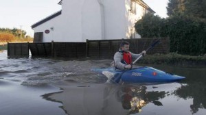 A man paddles his canoe on a flooded property in Yalding