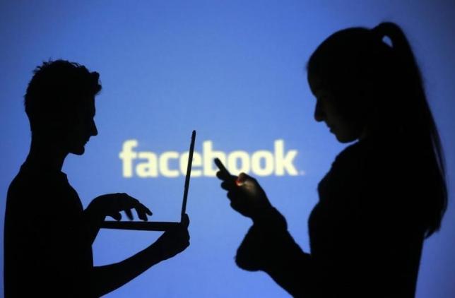 People pose with laptops in front of projection of Facebook logo in this picture illustration taken in Zenica