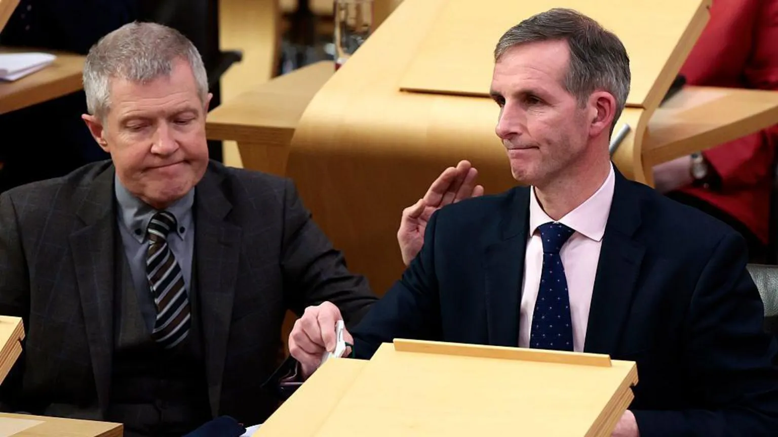 Getty Images Liam McArthur, a man with greying hair, wearing a dark suit and pink shirt, sits in the Holyrood chamber looking despondent. He is being patted on the shoulder by Willie Rennie, a man with grey hair, a grey three-piece suit and grey shirt.