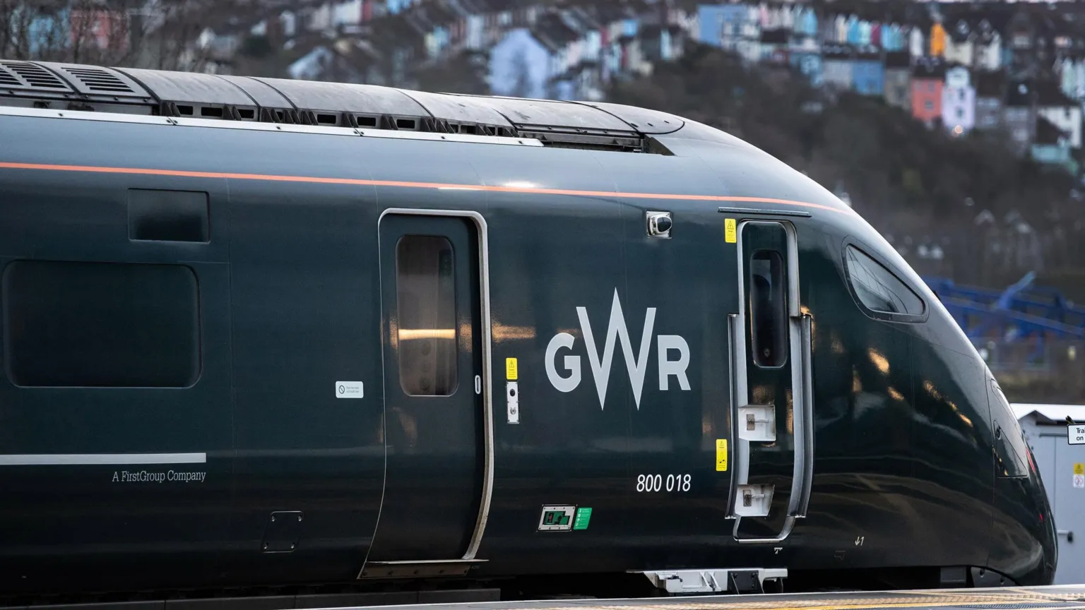 Great Western Railway A green train at a platform, with colourful houses slightly out of focus in the background.