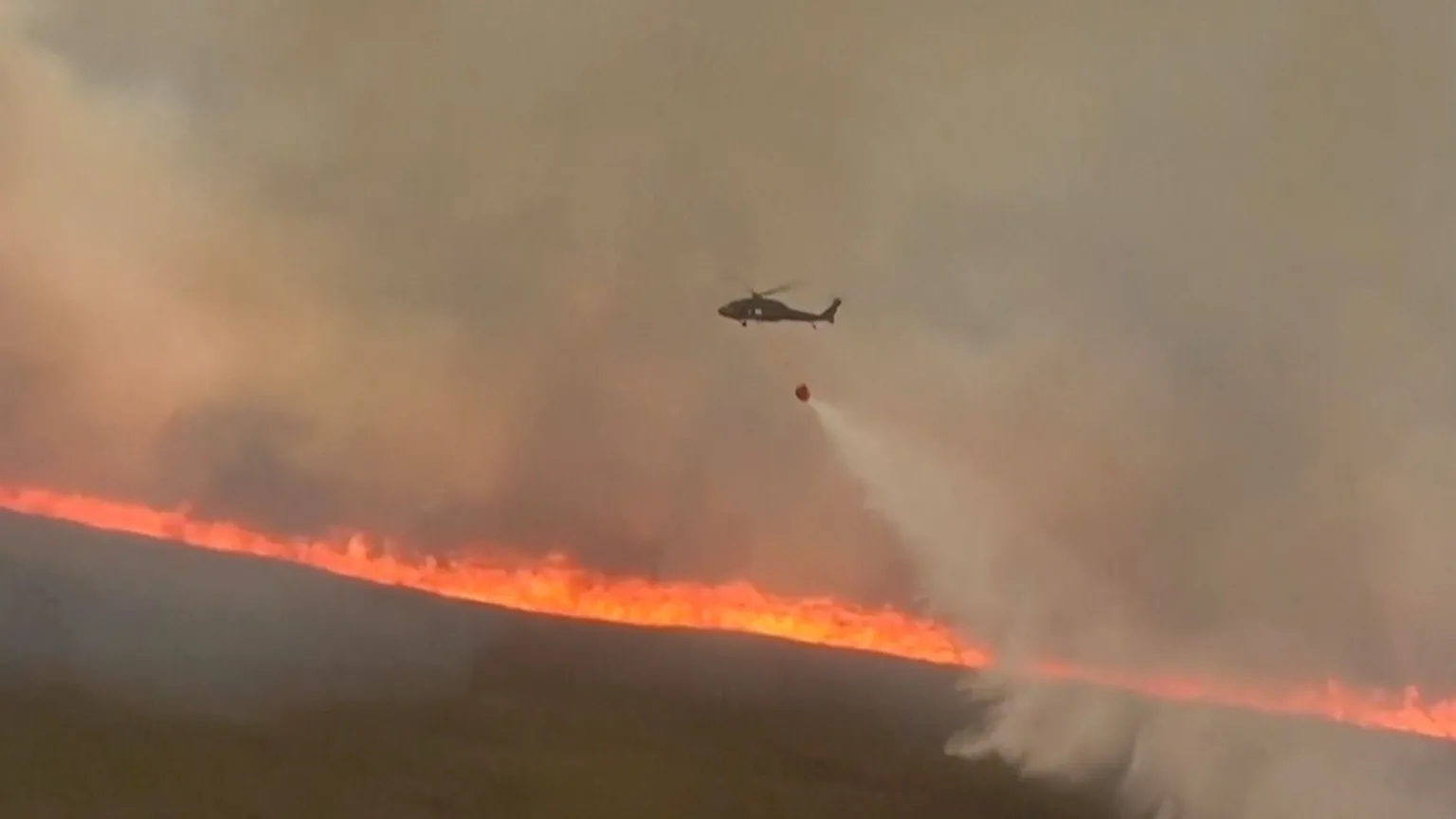 A lone helicopter carries a water bucket across the Everglades fire.