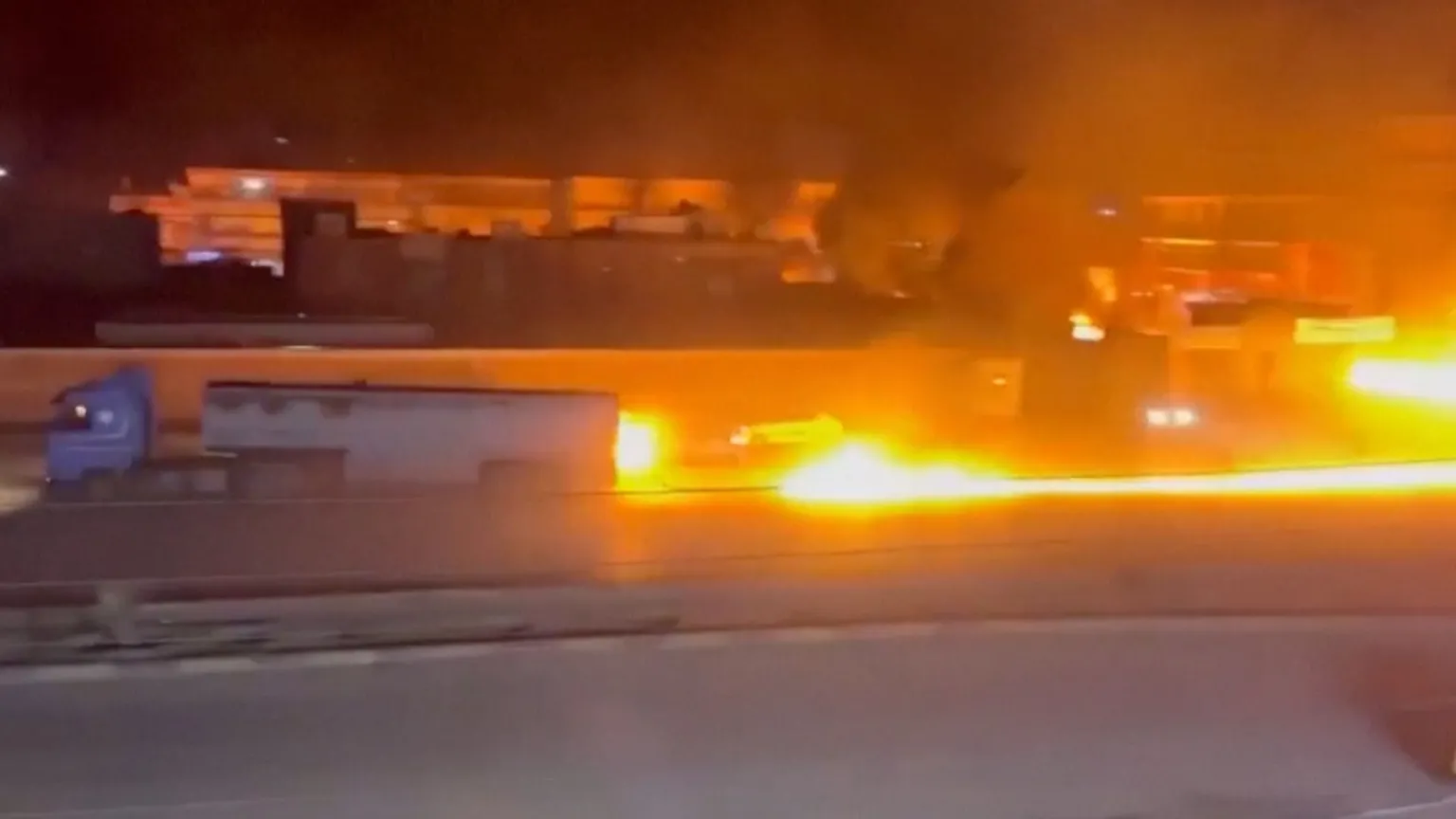 A fuel tanker truck driving with a long line of fire behind it.