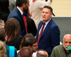 A high-angle shot of Wes Streeting looking agape across a crowd of people at an election count