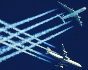 Two airliners flying at high altitude against a deep blue sky, leaving multiple white contrails behind them.