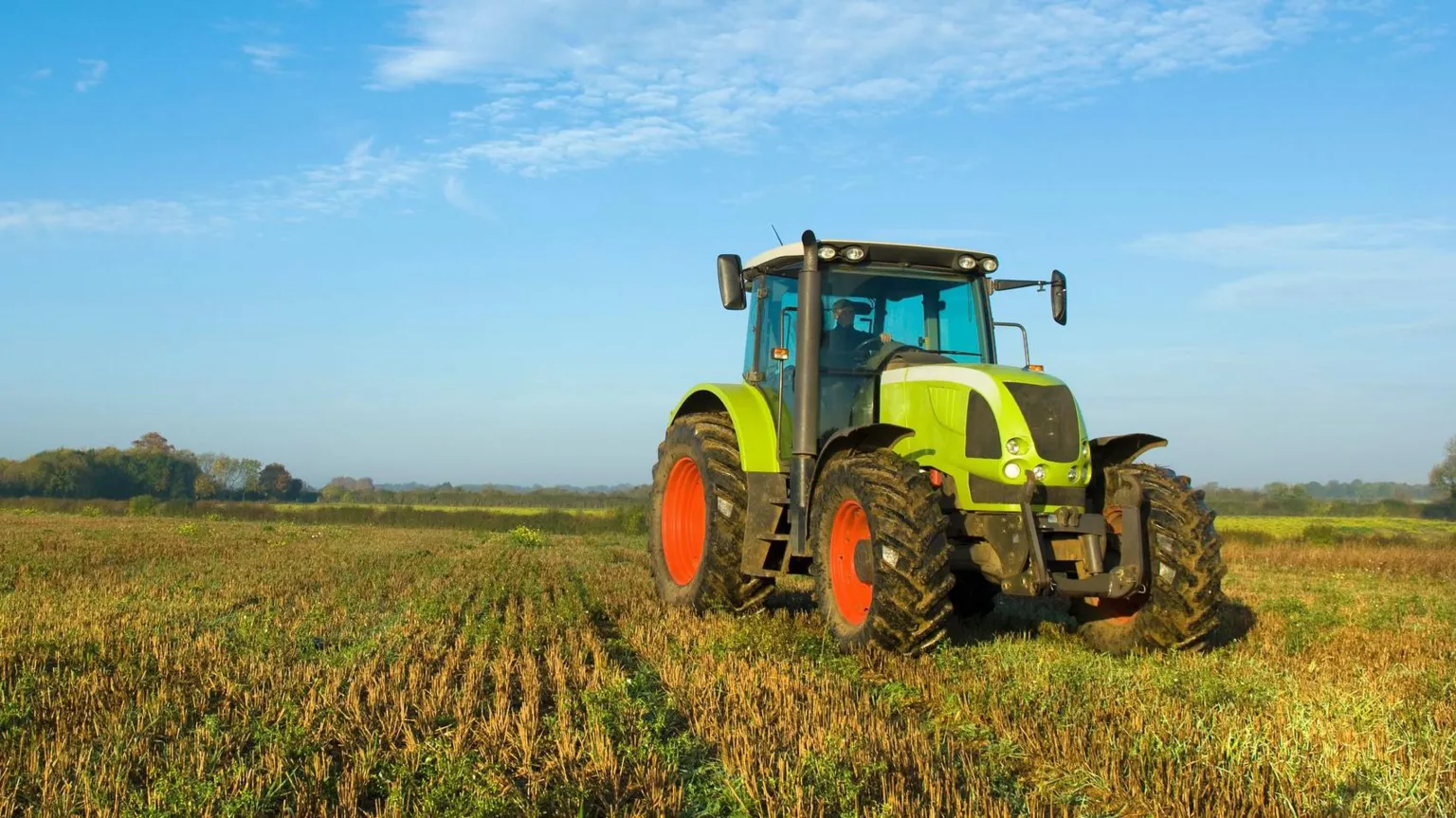 A green tractor with large red wheels parked in a field