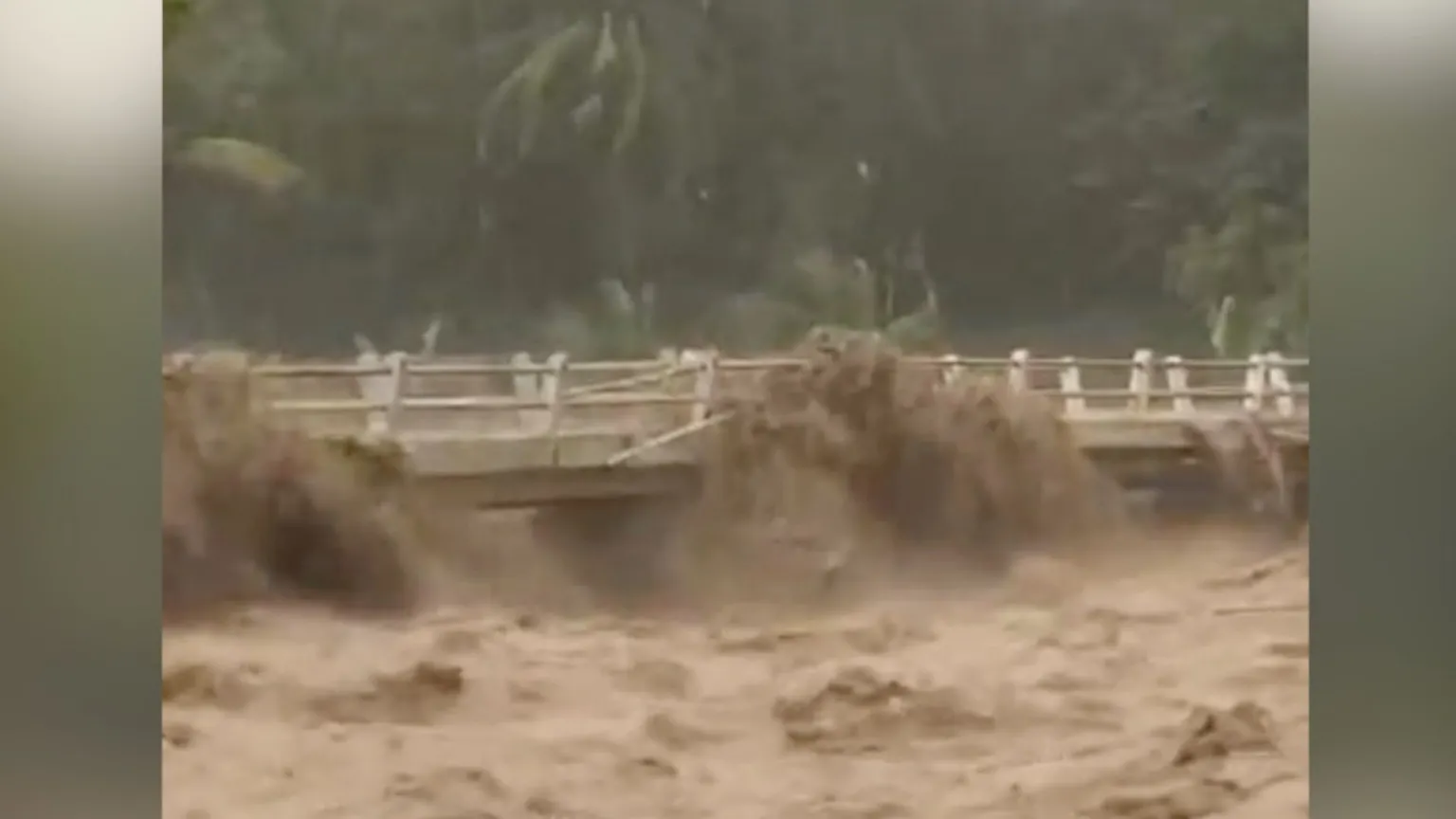 A muddy river rises up to a white bridge.