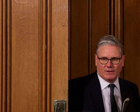 Keir Starmer beside a wooden panelled door.