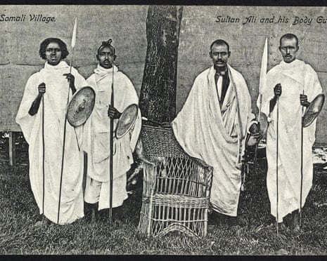 A black-and-white photo of Somali warriors posing next to a wicker chair