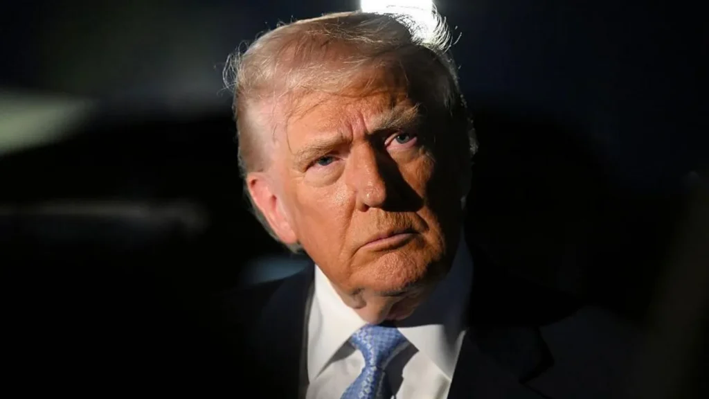 Getty Images Trump wearing a black suit and blue tie looks into the distance. The background is black.