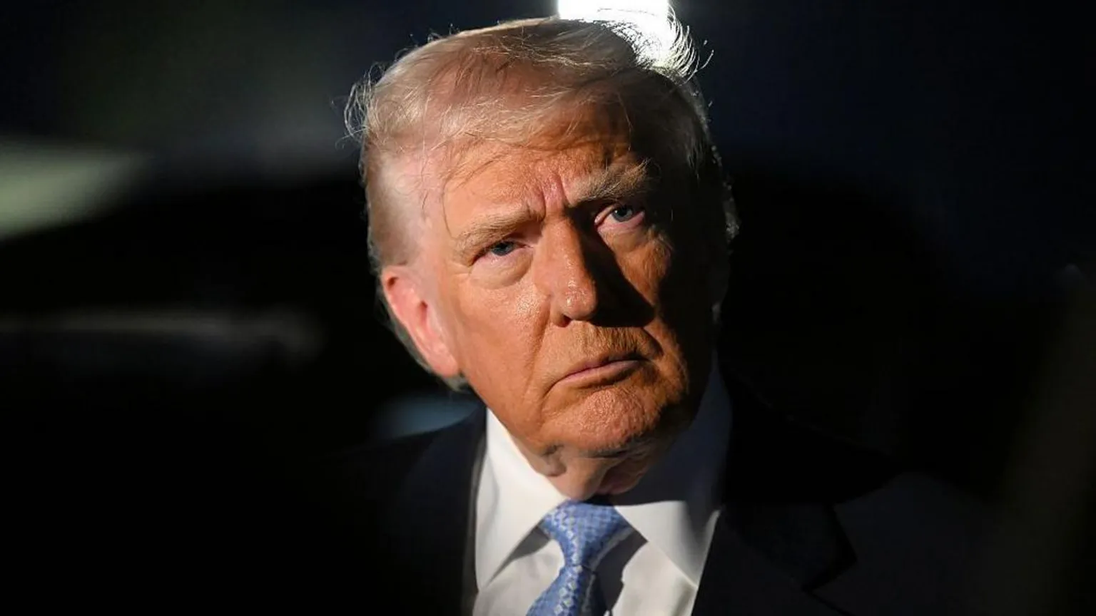Getty Images Trump wearing a black suit and blue tie looks into the distance. The background is black.