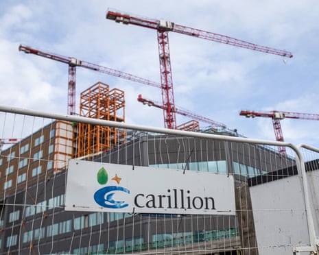 A Carillion sign on a fence in front of a construction site with red tower cranes and scaffolding above