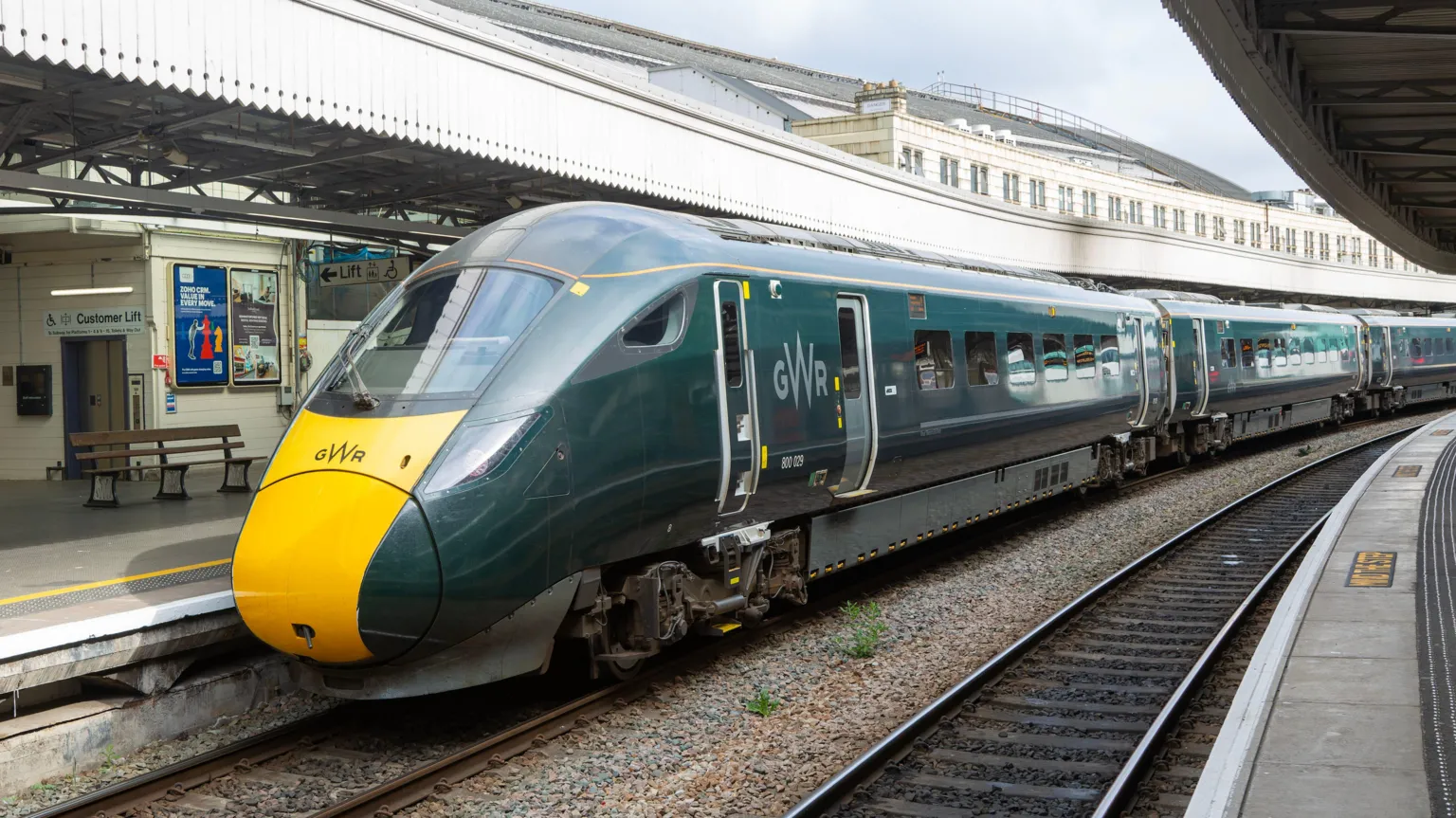 A Great Western Railway train at a platform in Bristol Temple Meads station. It is green and yellow and has GWR branding on the front and side.