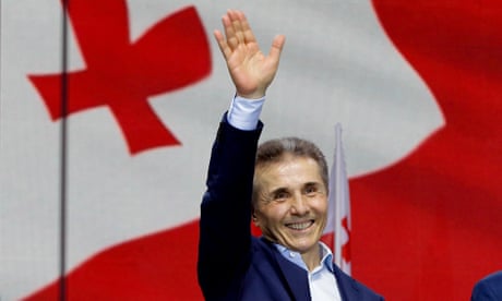 Bidzina Ivanishvili waves to a crowd in front of a Georgian flag