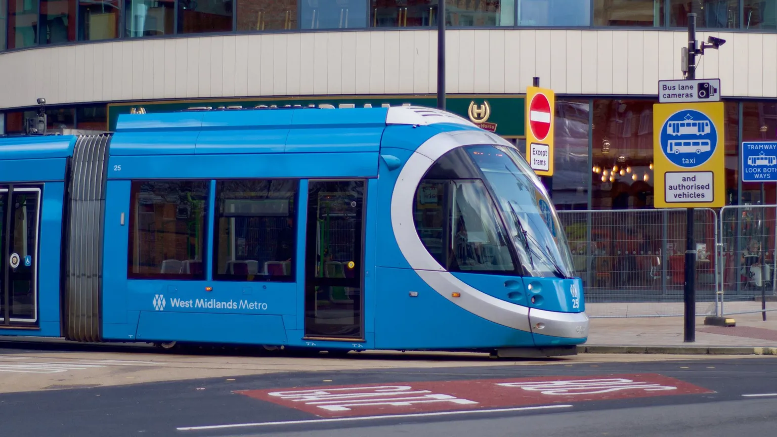 A blue tram with West Midlands Metro on the side on a Wolverhampton street, with bus lane signs.