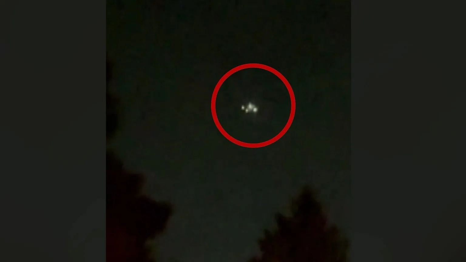 A drone circled with a red graphic flies over tree tops