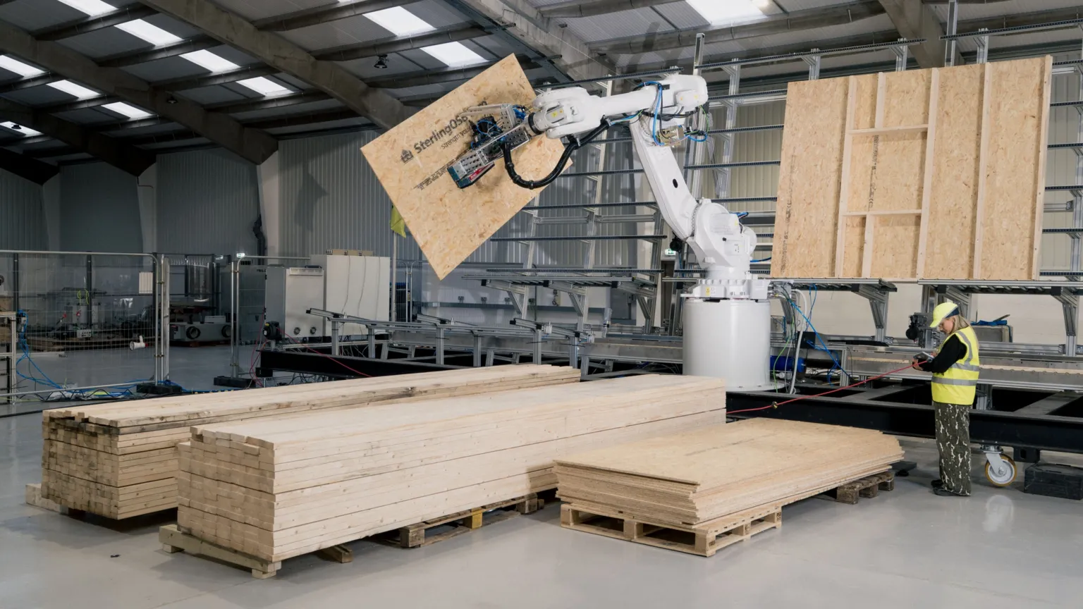 AUAR A large robot arm holds a wooden panel. Alongside is a worker in a hi-viz jacket.