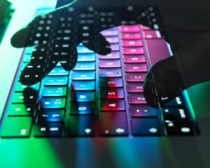 A shadowy translucent hand types on the keyboard of a laptop