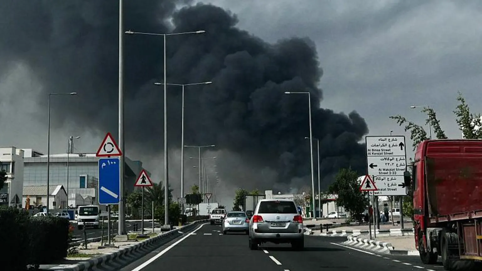 AFP via Getty Images Cars on a road in Qatar, as smoke billows into the sky after an alleged Iranian attack