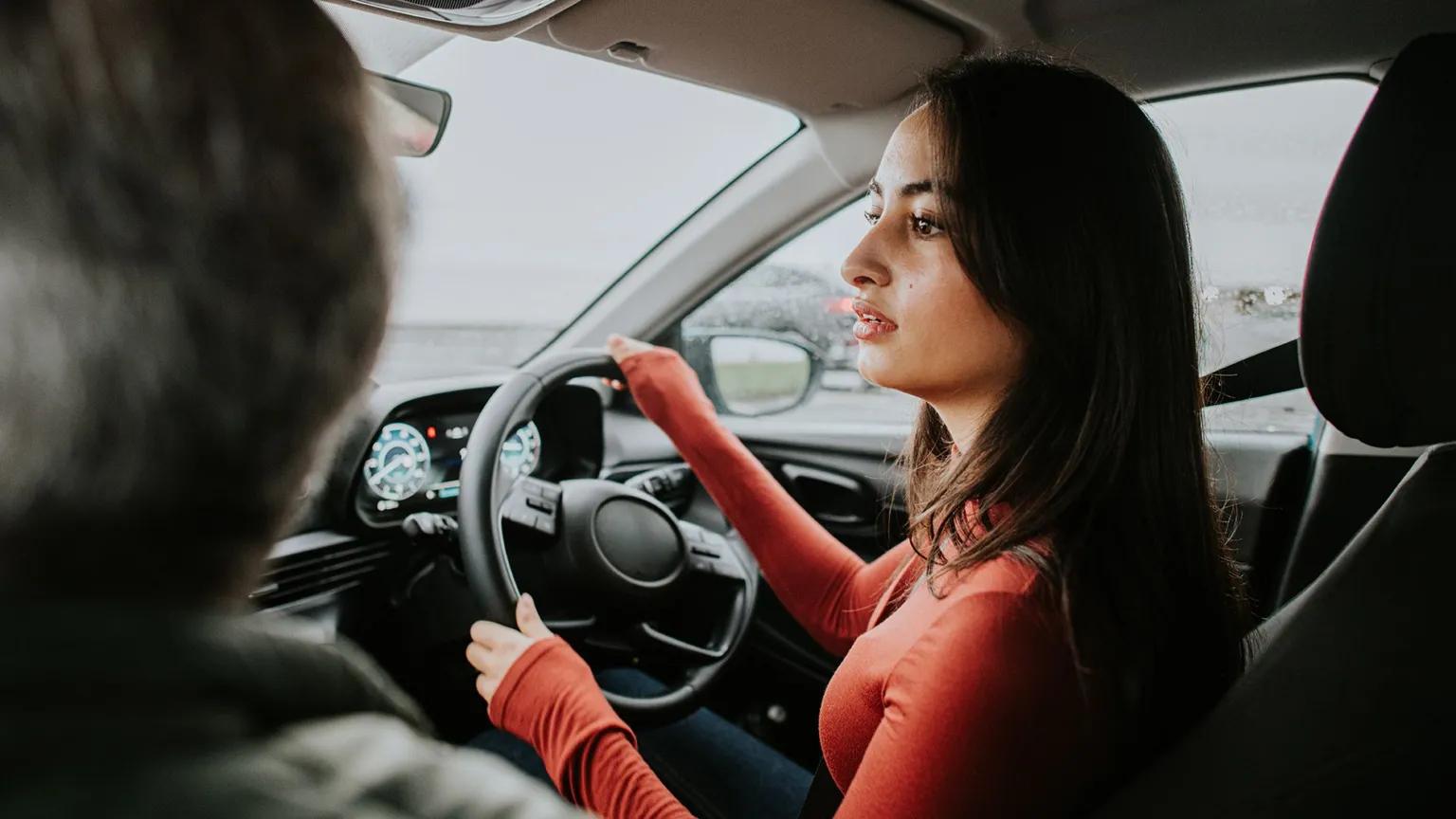 Getty Images Stock image shows a young person turning a steering wheel as they reverse in a car while an instructor (out of frame) sits in the passenger seat.