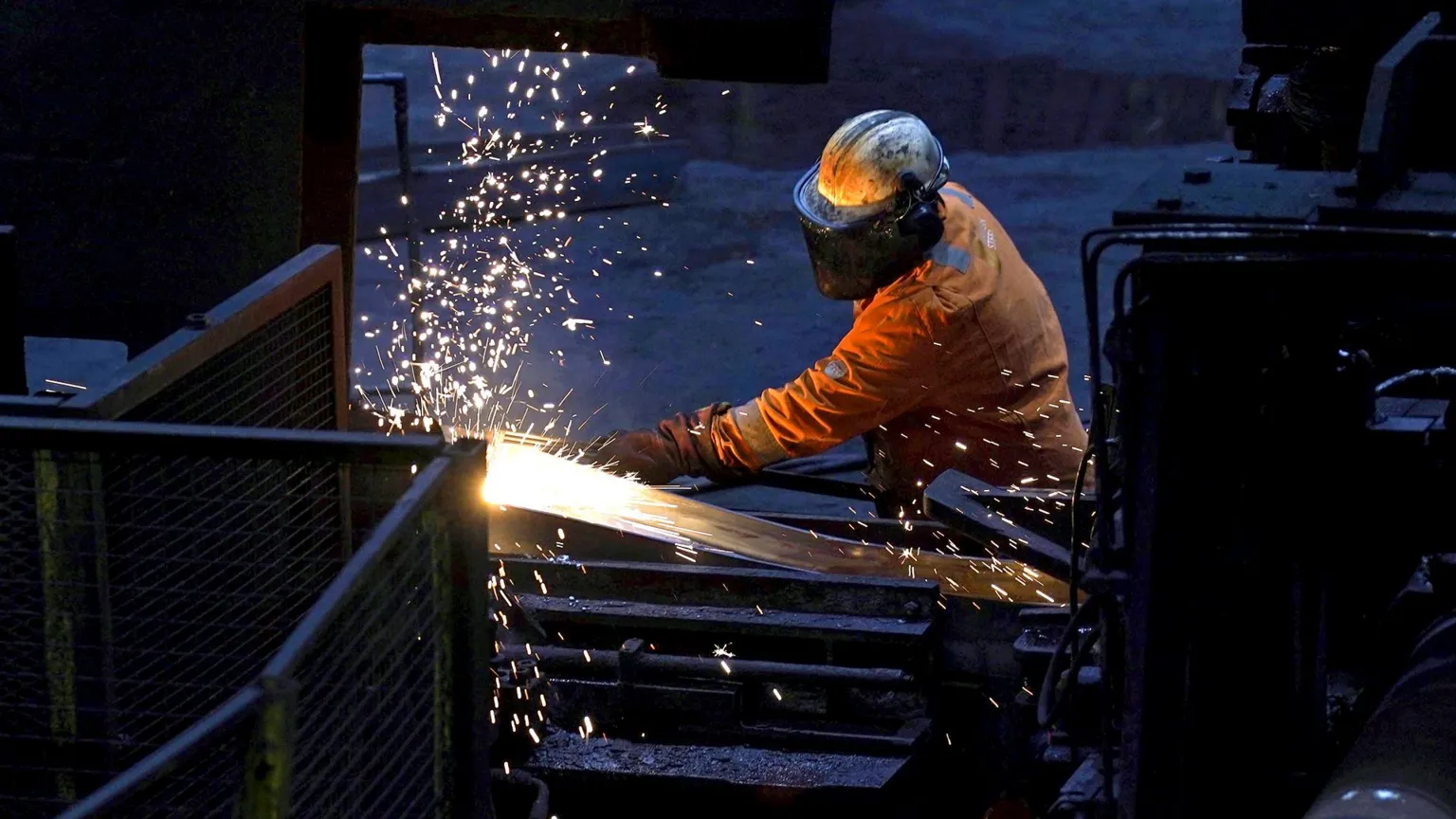 Danny Lawson / PA Media A steelworker wearing orange protective gear welds as sparks flies against a dark background in Scunthorpe Steel works in 2025.