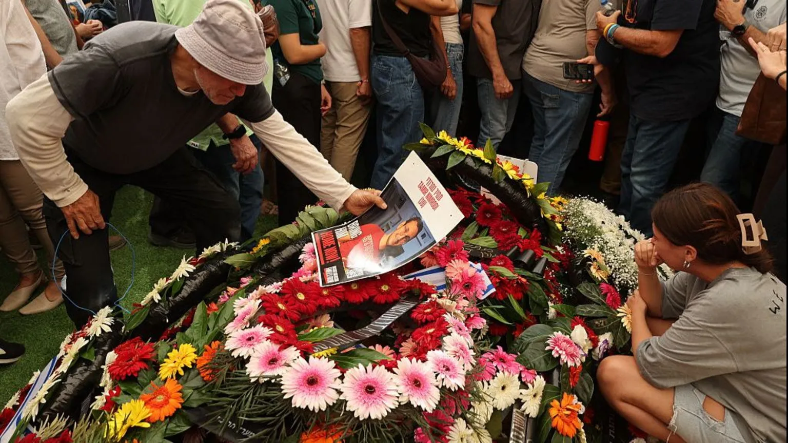 A man holds an image of Tamir Nimrodi, an Israeli soldier who died after being captured on 7 October, above a pile of flowers, surrounded by other mourners