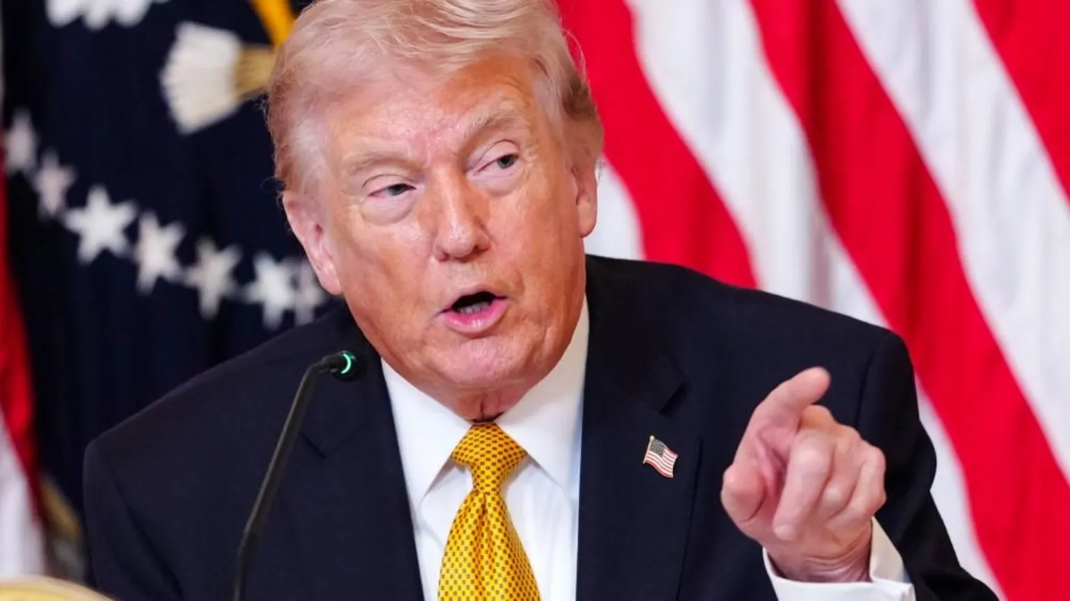 EPA/Shutterstock Donald Trump is pointing as he answers a question. He is wearing a dark coloured suit, white shirt and a yellow tie. He is also wearing a US flag badge on his lapel.