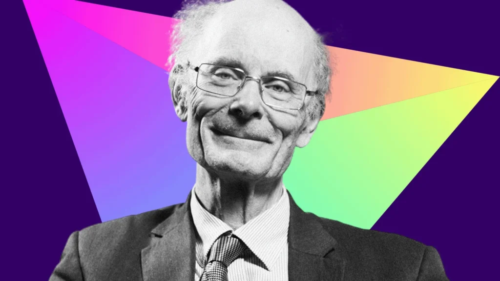 BBC Black and white photo of Prof Sir John Curtice who has a bald head with grey hair at the sides. He is wearing metal-rimmed glasses, a dark suit and tie and a light-coloured shirt. He is smiling at the camera. The background is a prism r triangle made up of different bright colours
