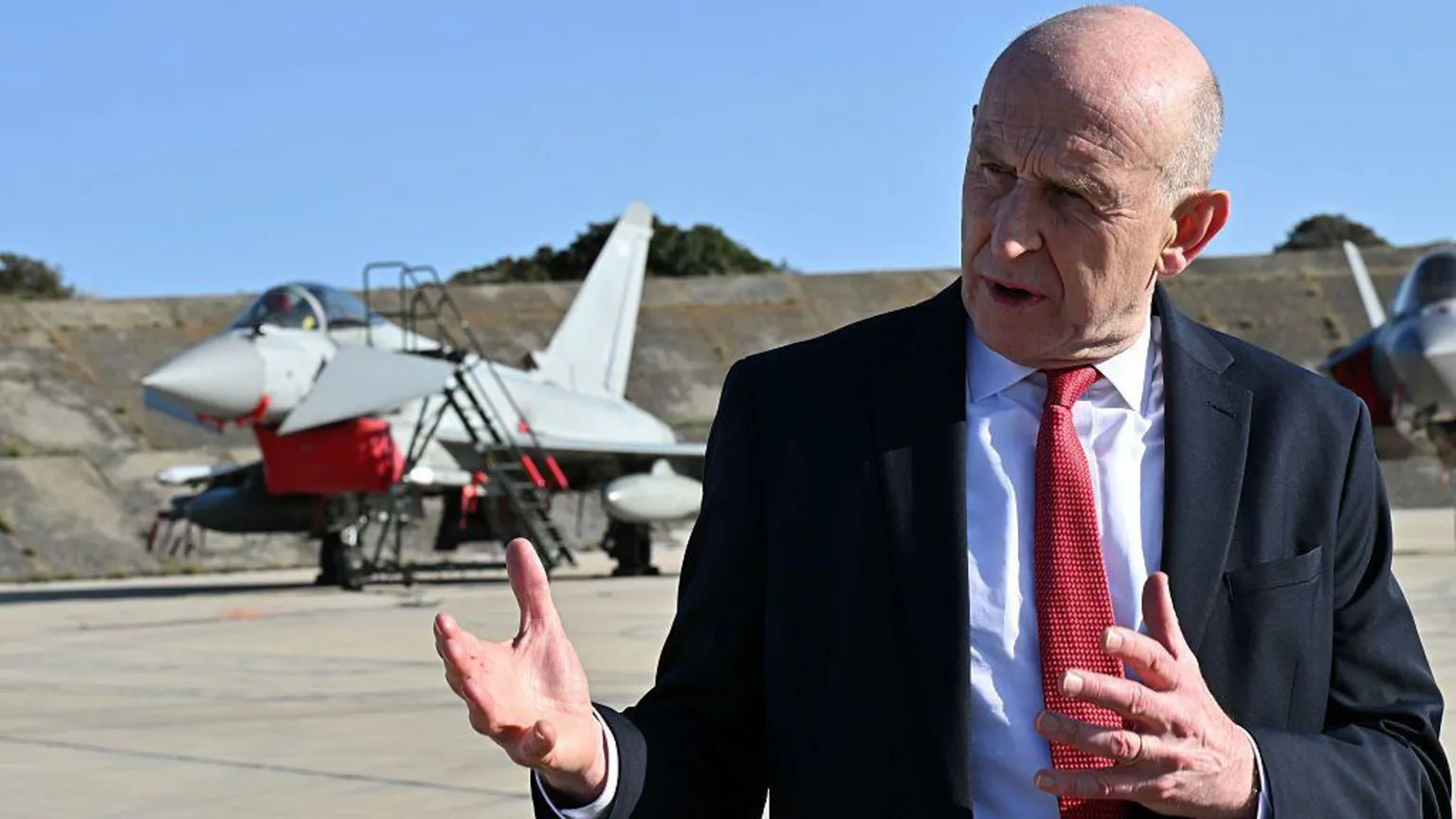 Leon Neal/Getty Images A man in a suit stands in front of a UK Typhoon jet