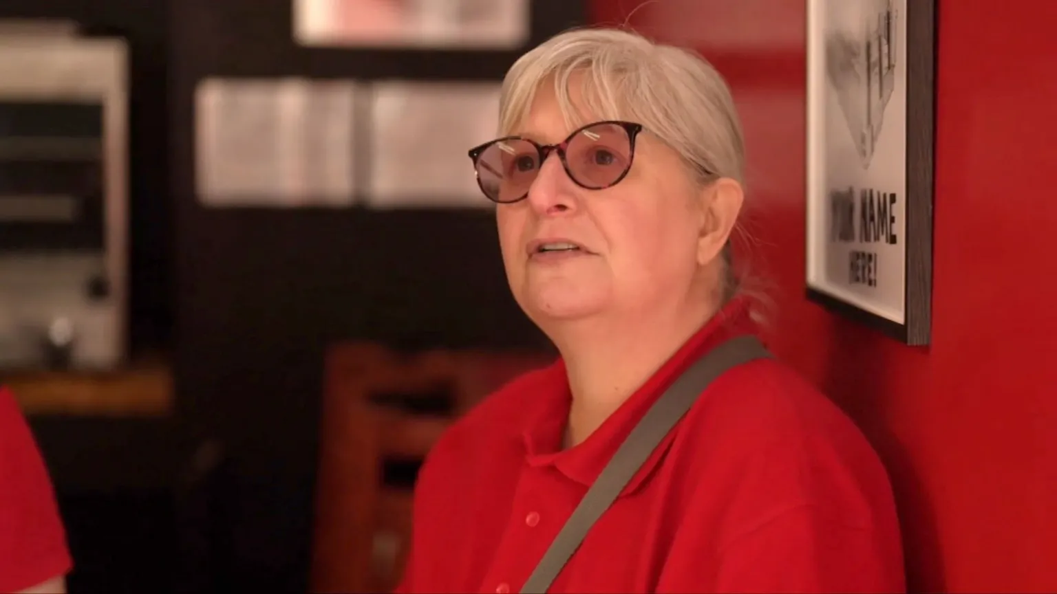 A woman wearing a red top answers questions inside a shop