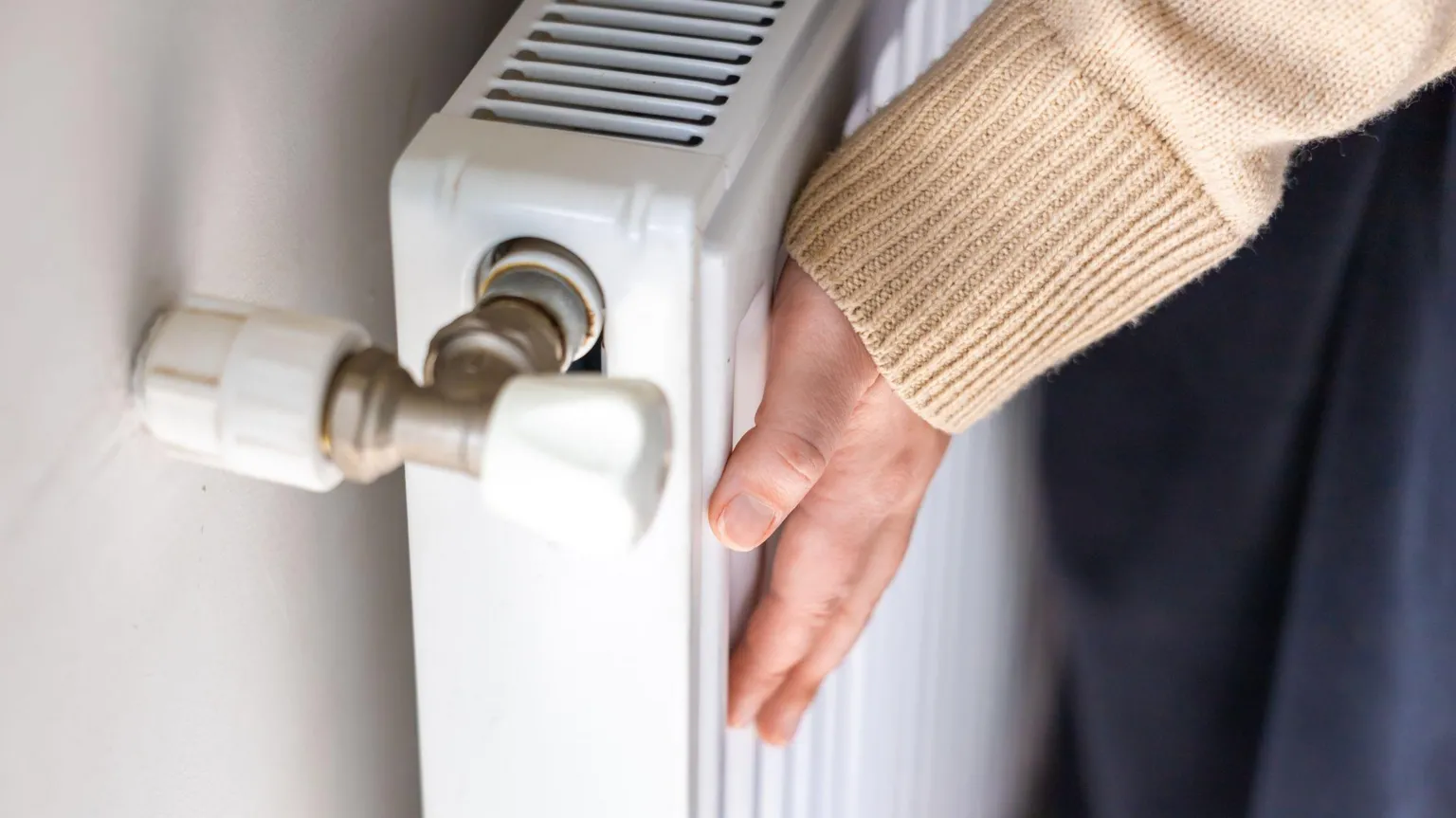 Getty Images A close-up image of a person's hand touching the panel of a white radiator.