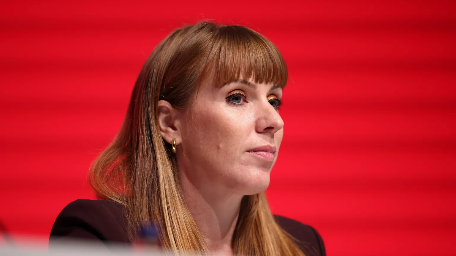 EPA Angela Rayner wearing a mauve blazer against a red background. She has long auburn hair and a fringe.
