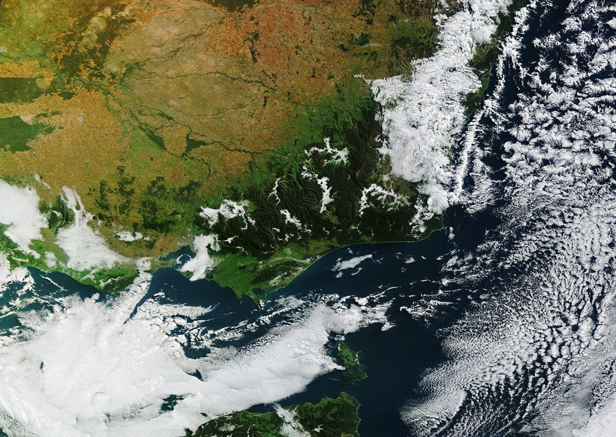 Wide patches of fog fill river valleys cutting through rugged, dark green mountains in eastern Victoria.