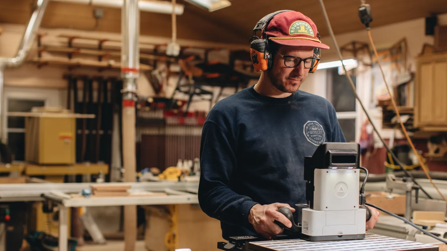 Shaper A man wearing a baseball cap and safety glasses uses a handheld router.