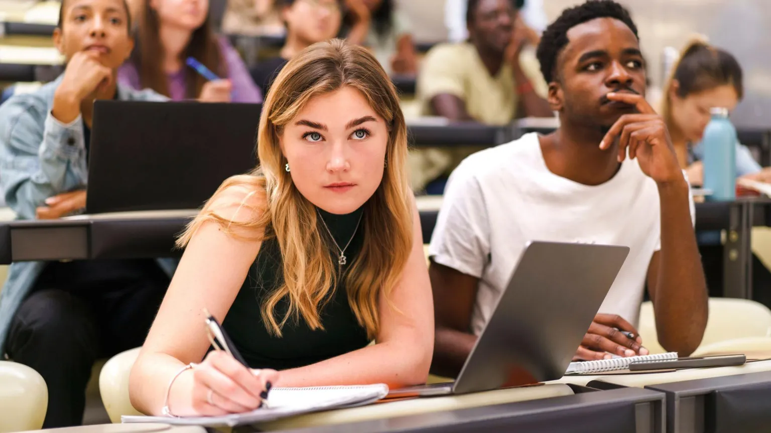 A stock photo of students in a classroom, with one woman jotting in her notepad