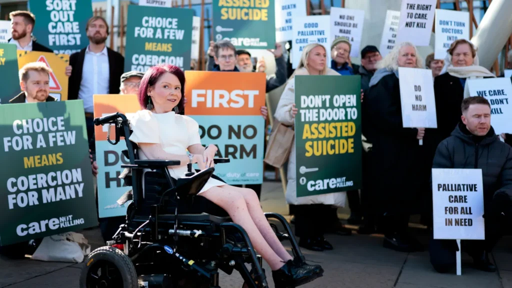 Getty Images A woman in a wheelchair in front of a group of protesters holding placards arguing against assisted dying