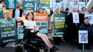 Getty Images A woman in a wheelchair in front of a group of protesters holding placards arguing against assisted dying