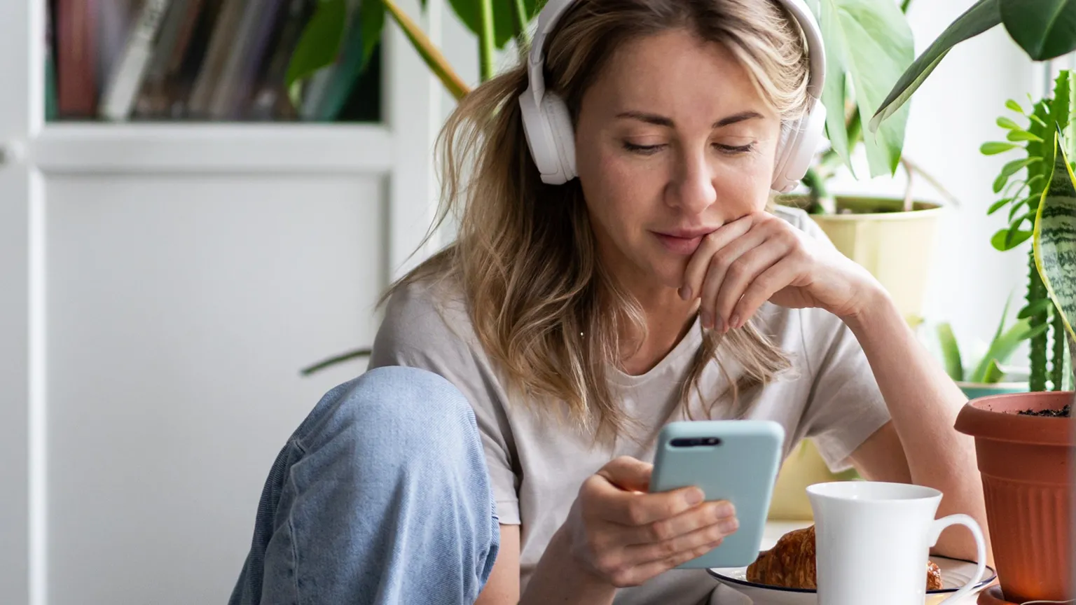 Getty Images A stock shot of a young blonde woman wearing white headphone and looking at her phone.