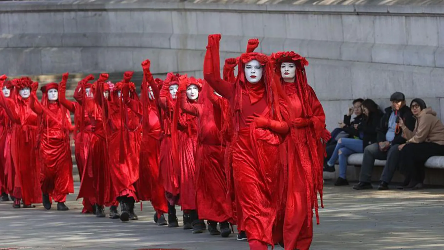 Getty Images A line of women dress in red, each with a fist raised, protest in London against new oil and gas fields