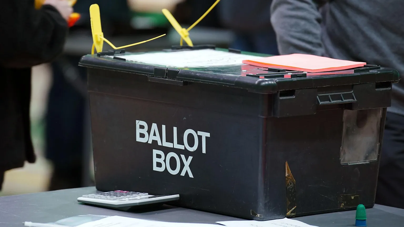 A dark ballot box with yellow tags.