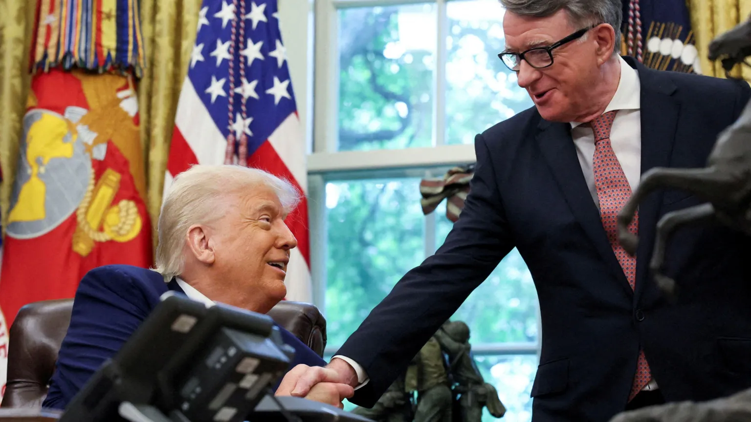 Reuters Lord Mandelson shakes hands with US President Donald Trump in the Oval Office at the White House in May 2025. President Trump is sitting in a chair, while Lord Mandelson stands in front of a window and a US flag.