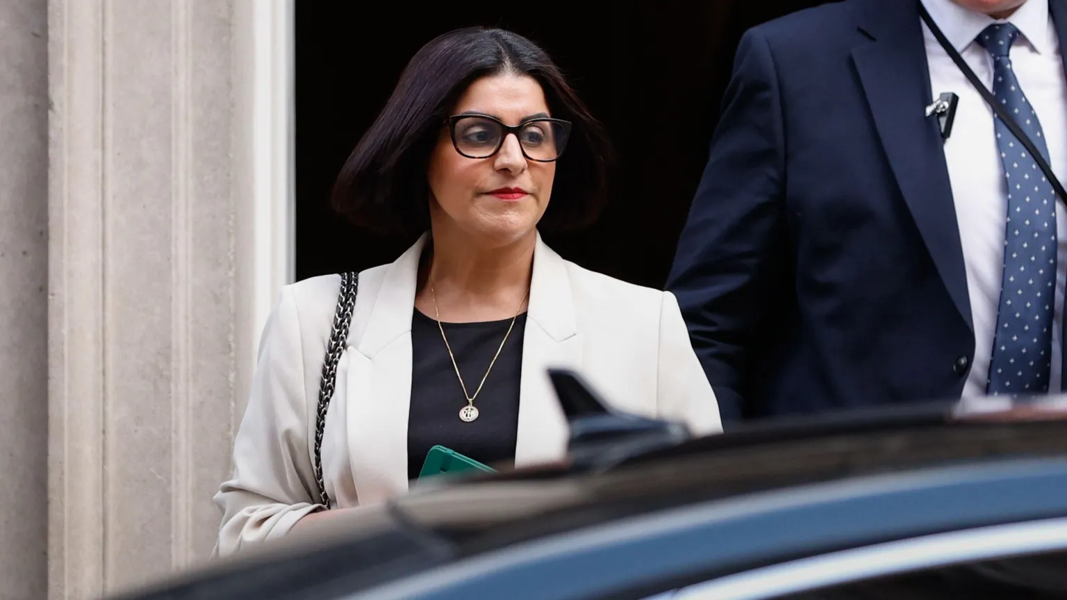 EPA Home Secretary Shabana Mahmood walking to a car wearing dark brown glasses, red lipstick, and a light grey blazer.