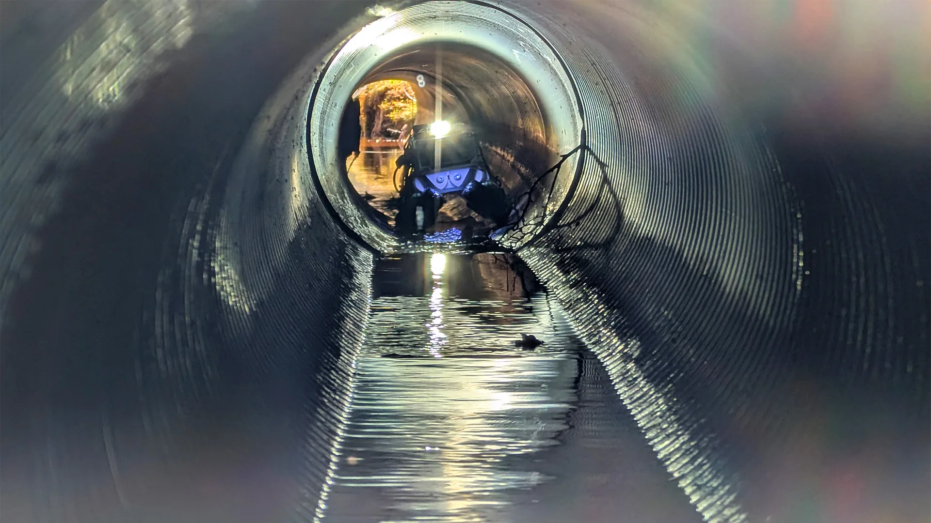 An autonomous inspection robot at one end of a long sewer pipe with water running along the bottom section (Credit: Pipeon project)